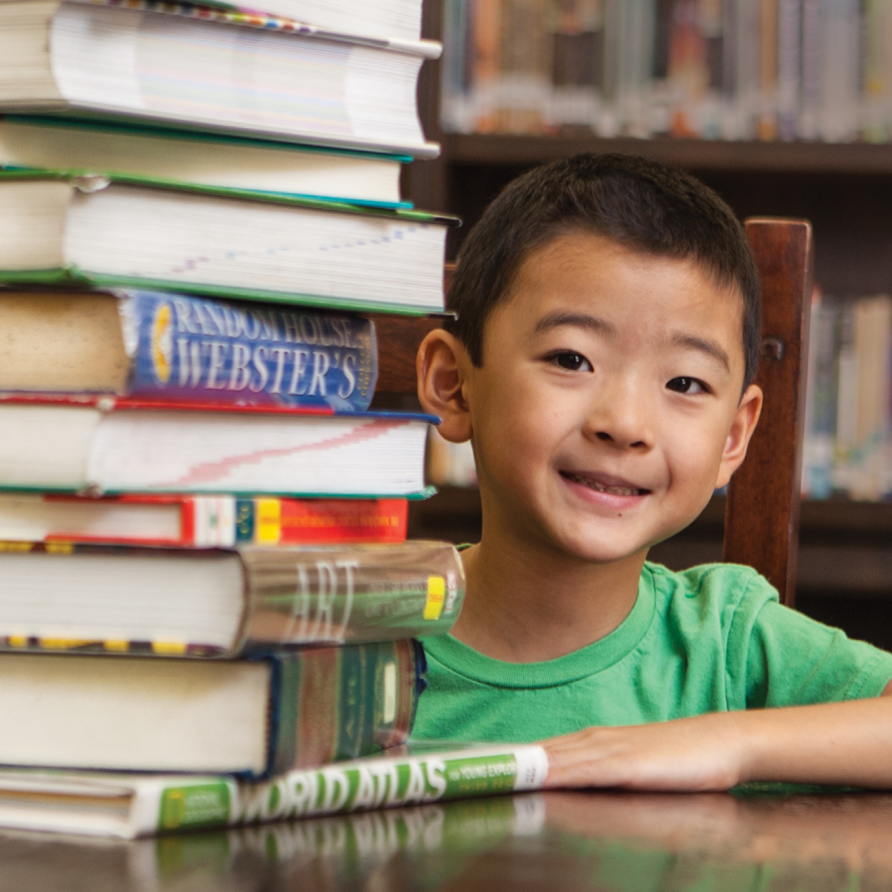 Boy with books sitting at table in library